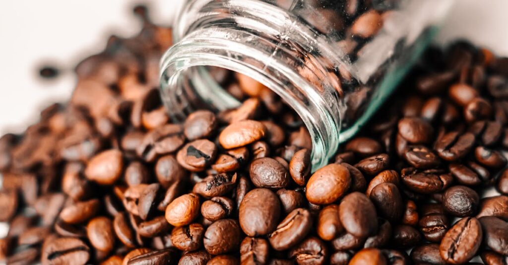 A detailed shot of aromatic coffee beans spilling from a transparent glass jar onto a surface.